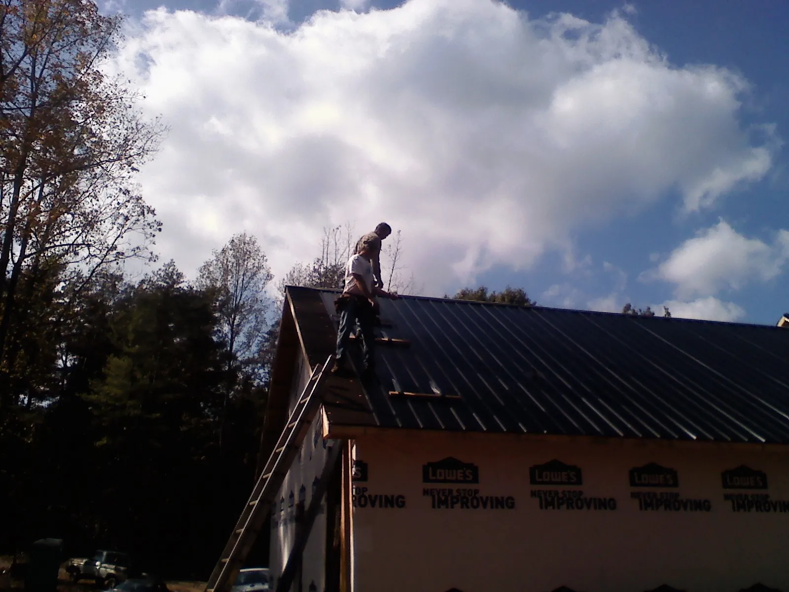 Roofer fastening dark metal panels high against a cloudy sky, from a Roof Inspection job in Wingdale