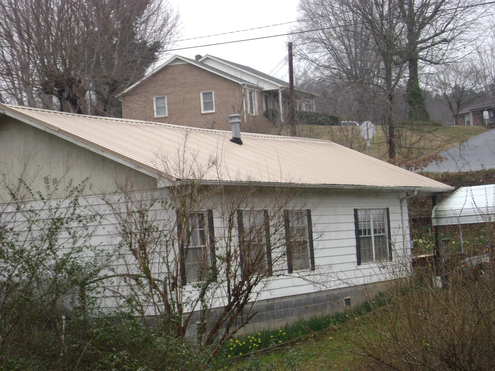 Tan metal roof on a white sided house set into a hillside — Commercial Roofing by Roofing Brothers in Wingdale